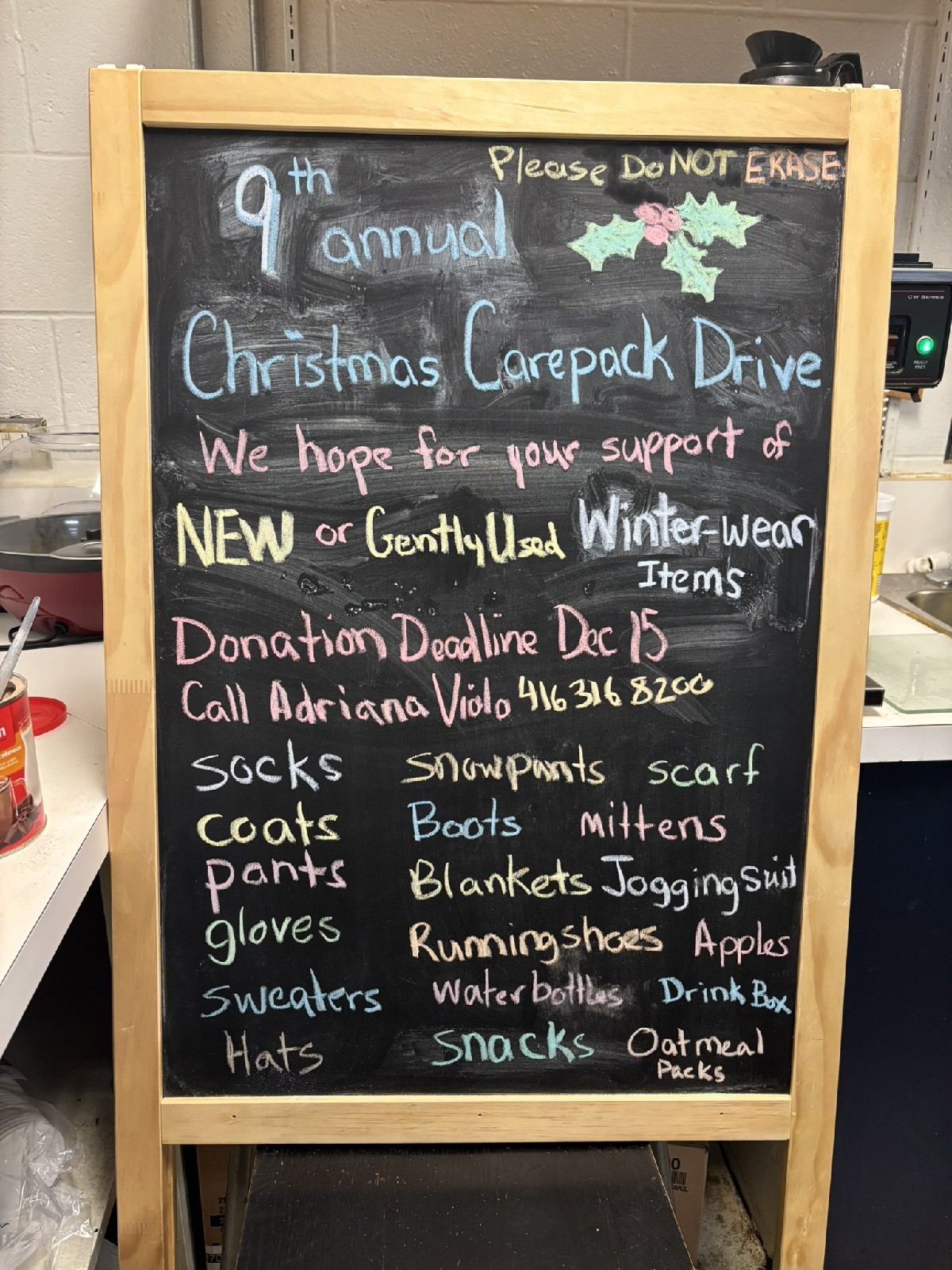 Hand-lettered chalkboard sign announcing the 9th annual Christmas Care Pack Drive, listing winter-wear items needed for donation